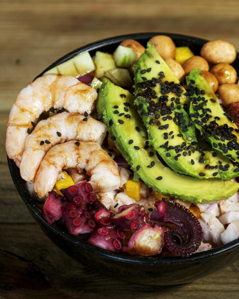 A vibrant seafood salad bowl with avocado, shrimp, and octopus, garnished with sesame seeds.