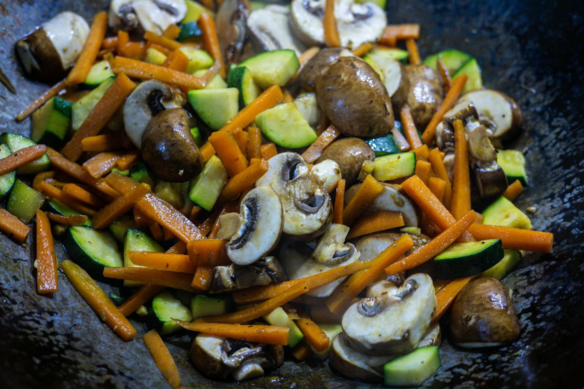 Close-up of vibrant stir-fried vegetables including mushrooms, carrots, and zucchini in a wok.